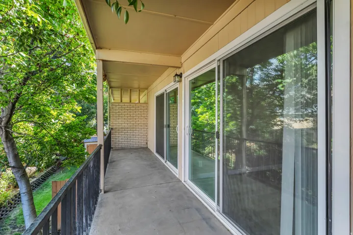 Covered concrete balcony with dark metal railings, light brick-finish wall, and multiple sliding glass doors