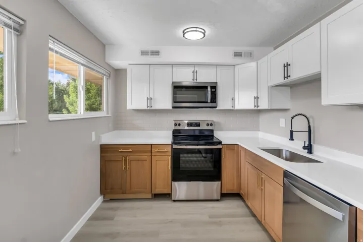 Modern kitchen featuring white upper cabinetry, natural wood-finish lower cabinetry, white countertops, stainless steel appliances, and wood-look flooring