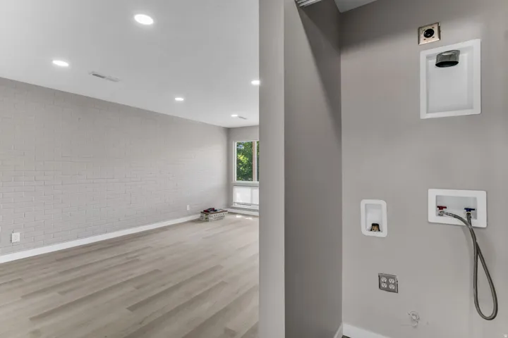 Laundry area with appliance hookups and a room featuring wood-finish flooring, a painted brick accent wall, recessed lighting, and a large window