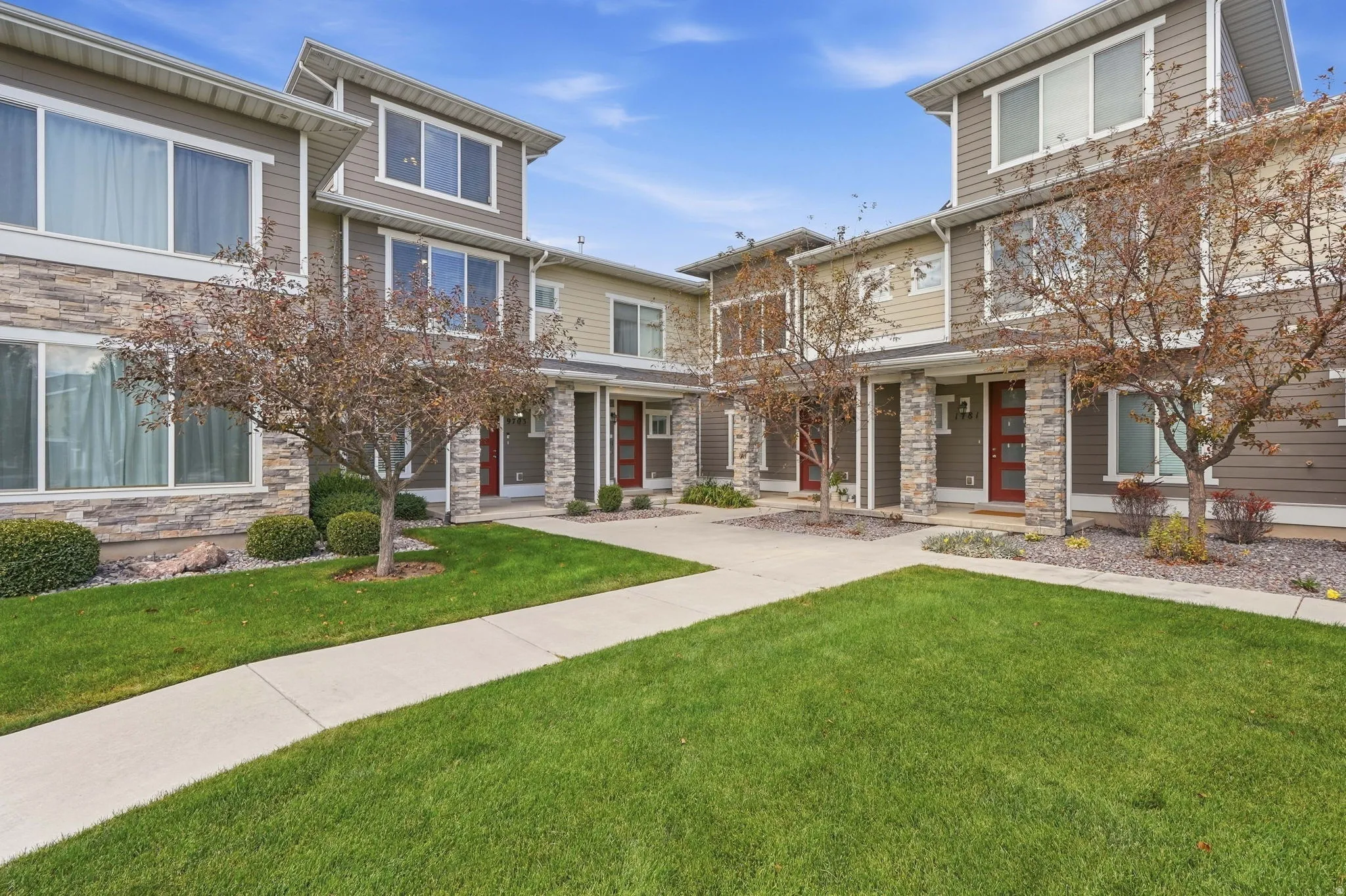 Contemporary townhome architecture featuring stacked stone accents, horizontal siding, multiple large windows, and a vibrant red entry door
