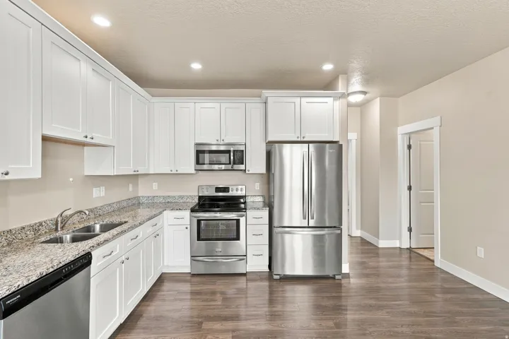 White shaker-style cabinetry, stainless steel appliances, granite-look countertops, dual basin sink, and wood-finish flooring
