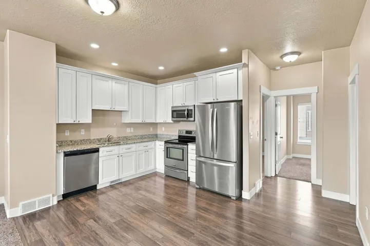 Kitchen featuring wood-finish flooring, white cabinetry, stainless steel appliances, and granite countertops