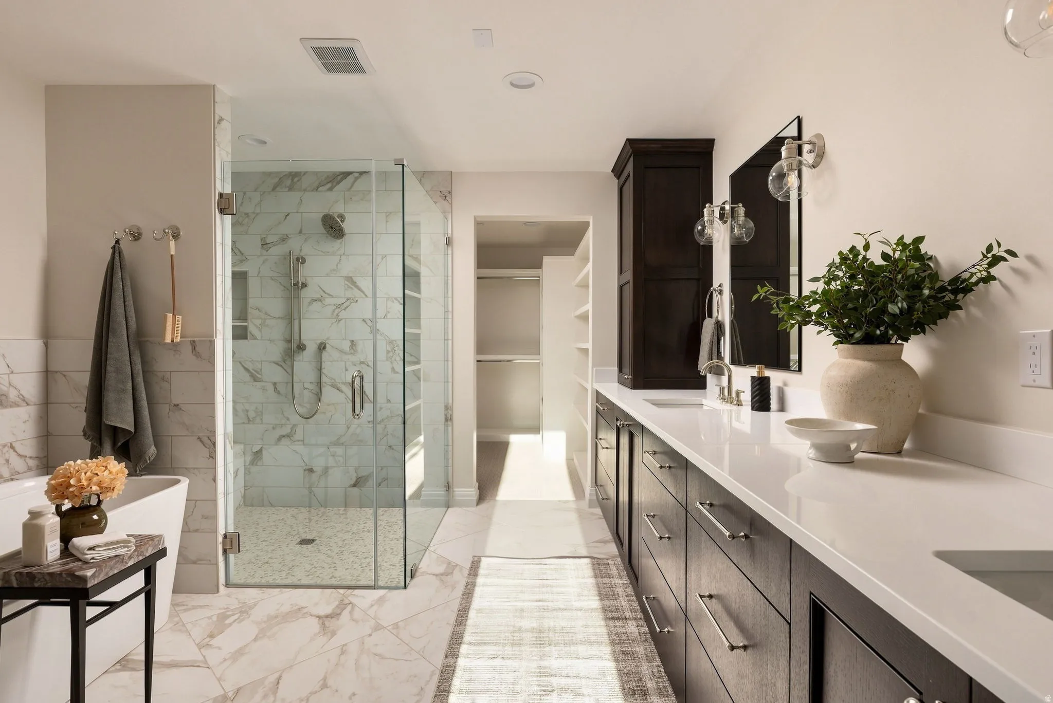Spacious bathroom featuring a freestanding tub, glass-enclosed shower with tiled walls, dual vanity with undermount sinks, stone countertops, and dark wood cabinetry