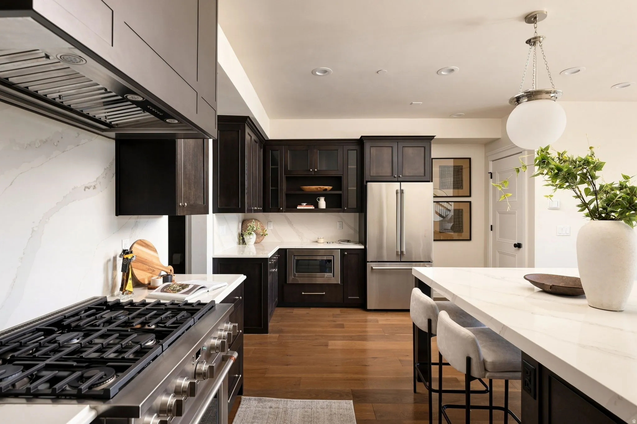 Gourmet kitchen featuring a stainless steel range, matching stainless steel appliances, dark wood cabinetry, white countertops with a matching backsplash, and hardwood flooring