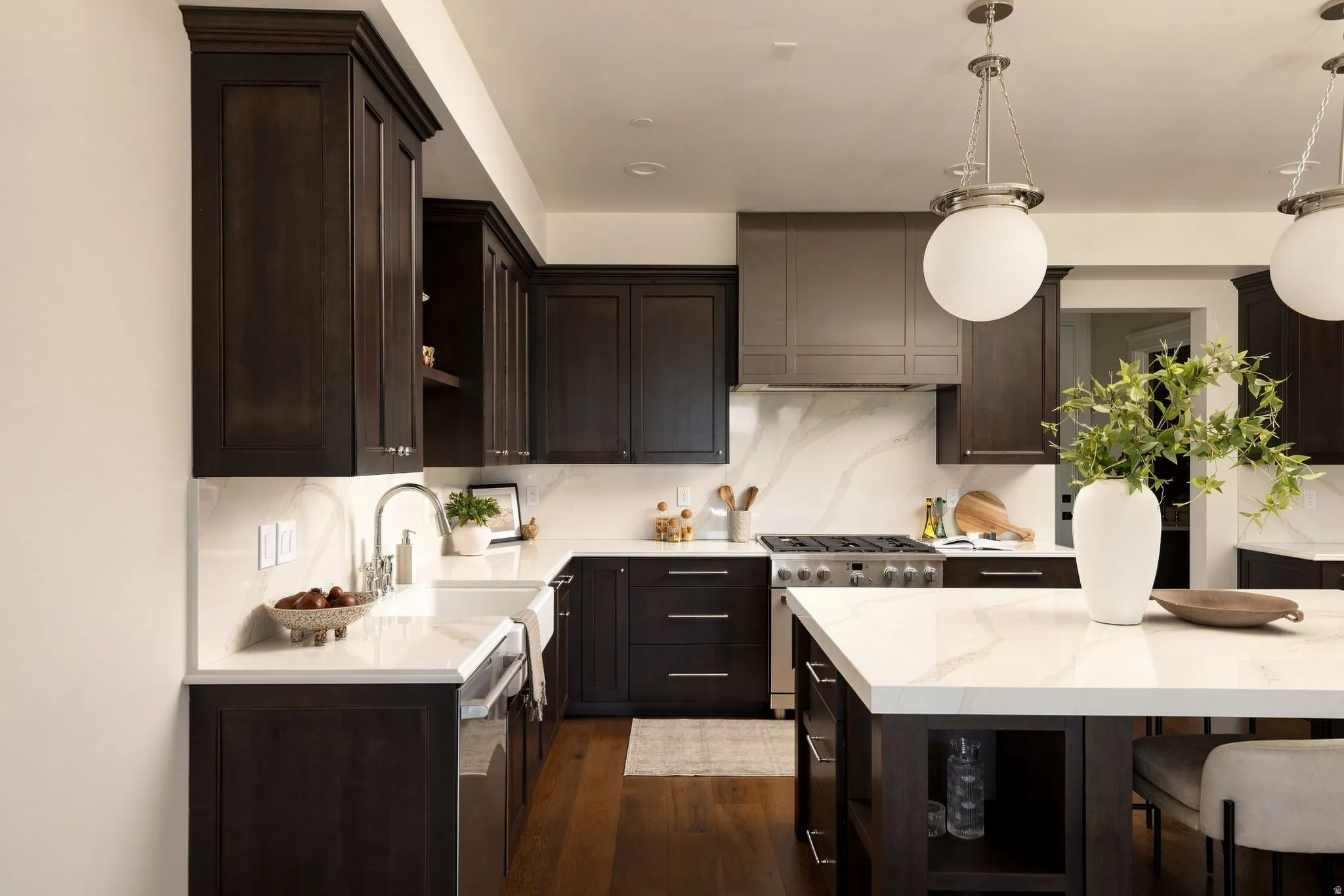 Kitchen featuring dark wood-finish cabinetry, white countertops with veining, a farmhouse sink, stainless steel range, and an island with pendant lighting