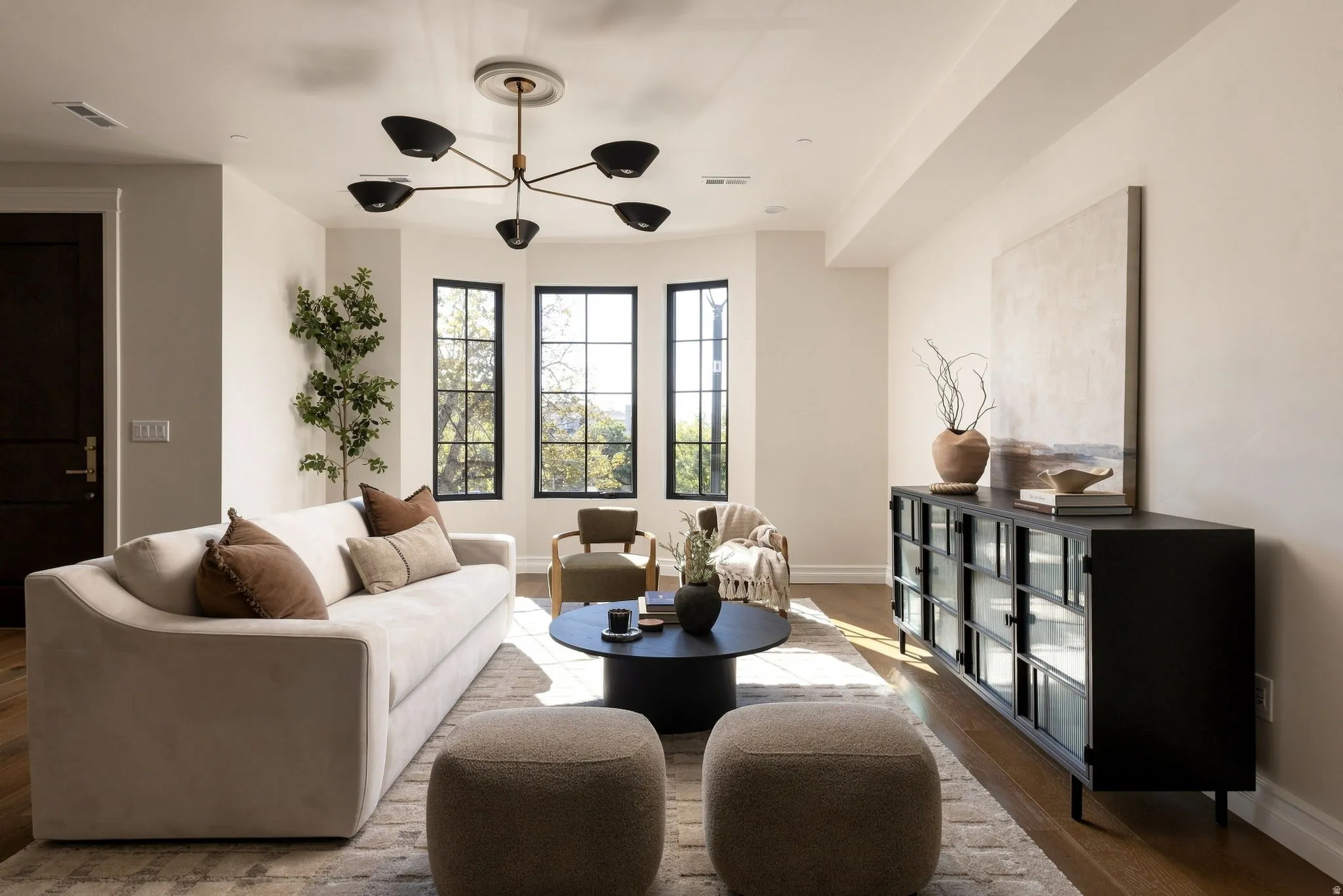 Expansive living area with wood-finish flooring, a modern chandelier, and a black-framed multi-pane window array