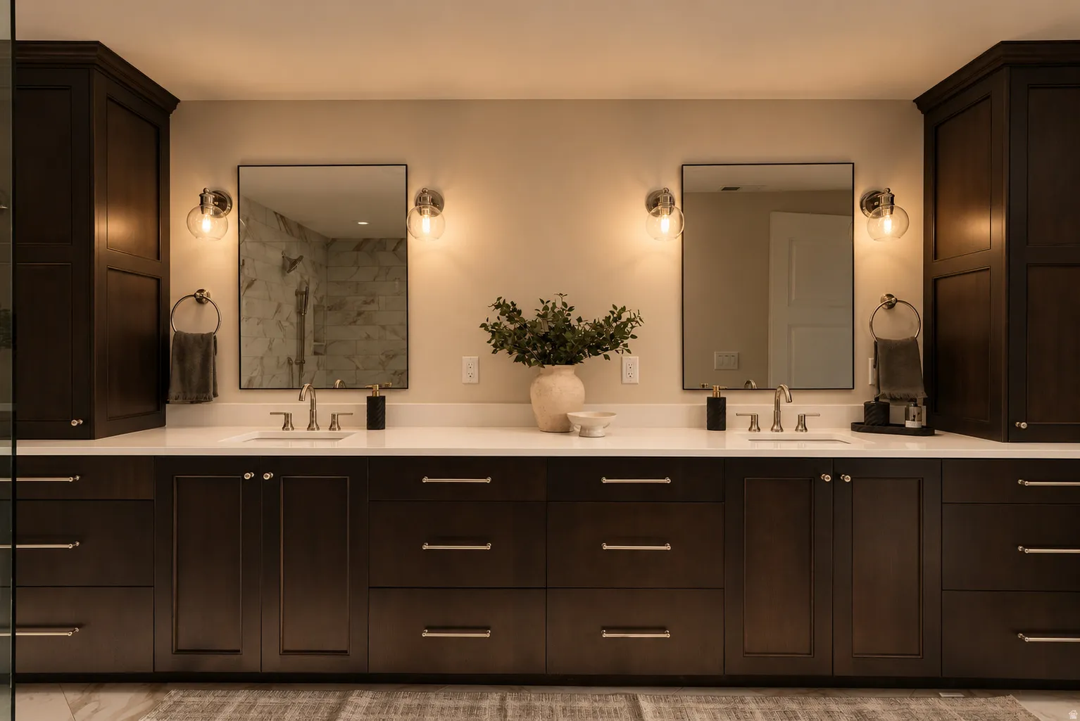 Dual vanity with wood-finish cabinetry, white countertops, rectangular undermount sinks, and wall-mounted sconces