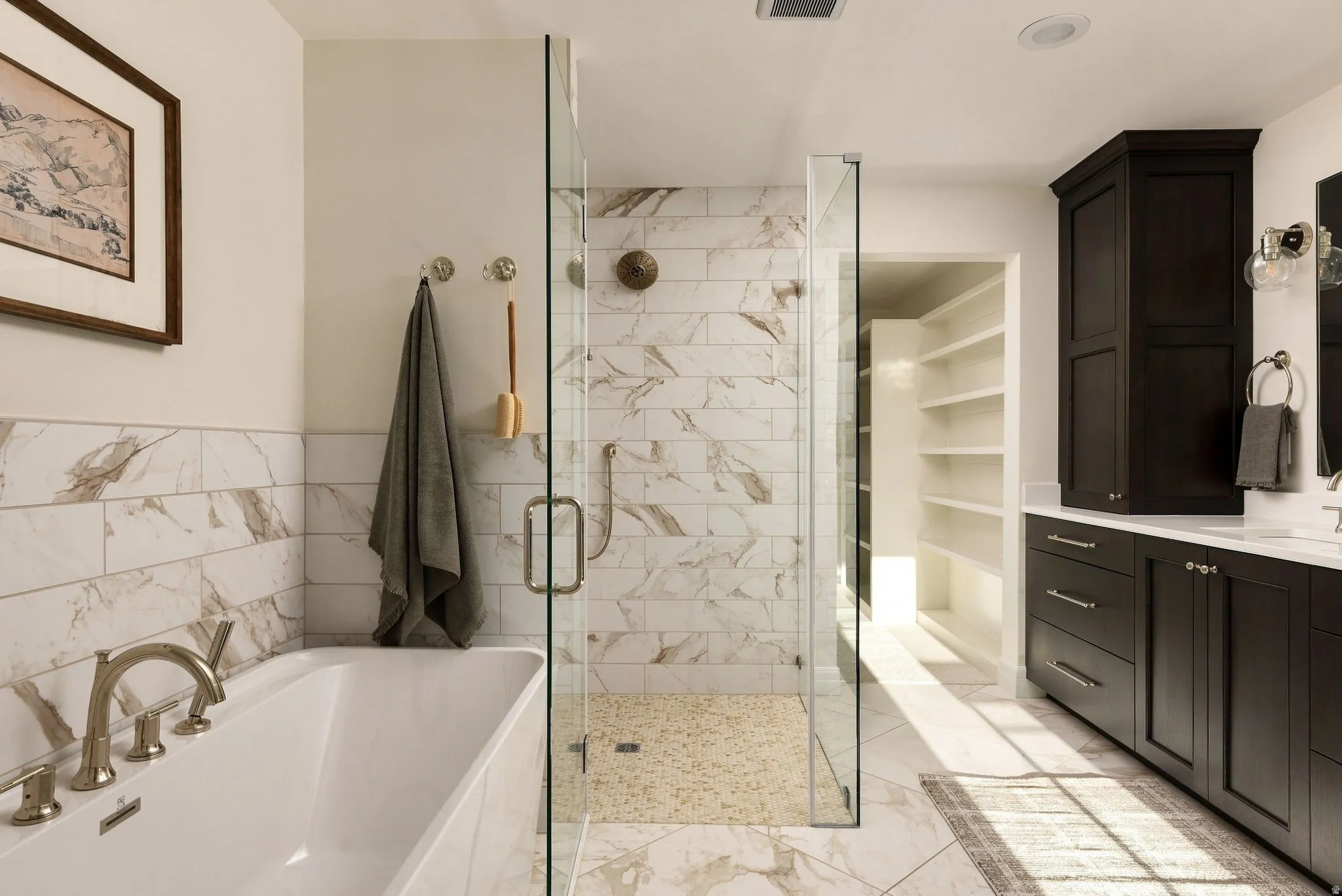 Spa-inspired primary bathroom showcasing marble-finish wall and floor tiling, a freestanding soaking tub with deck-mounted faucet, and a frameless glass-enclosed shower with rainfall showerhead