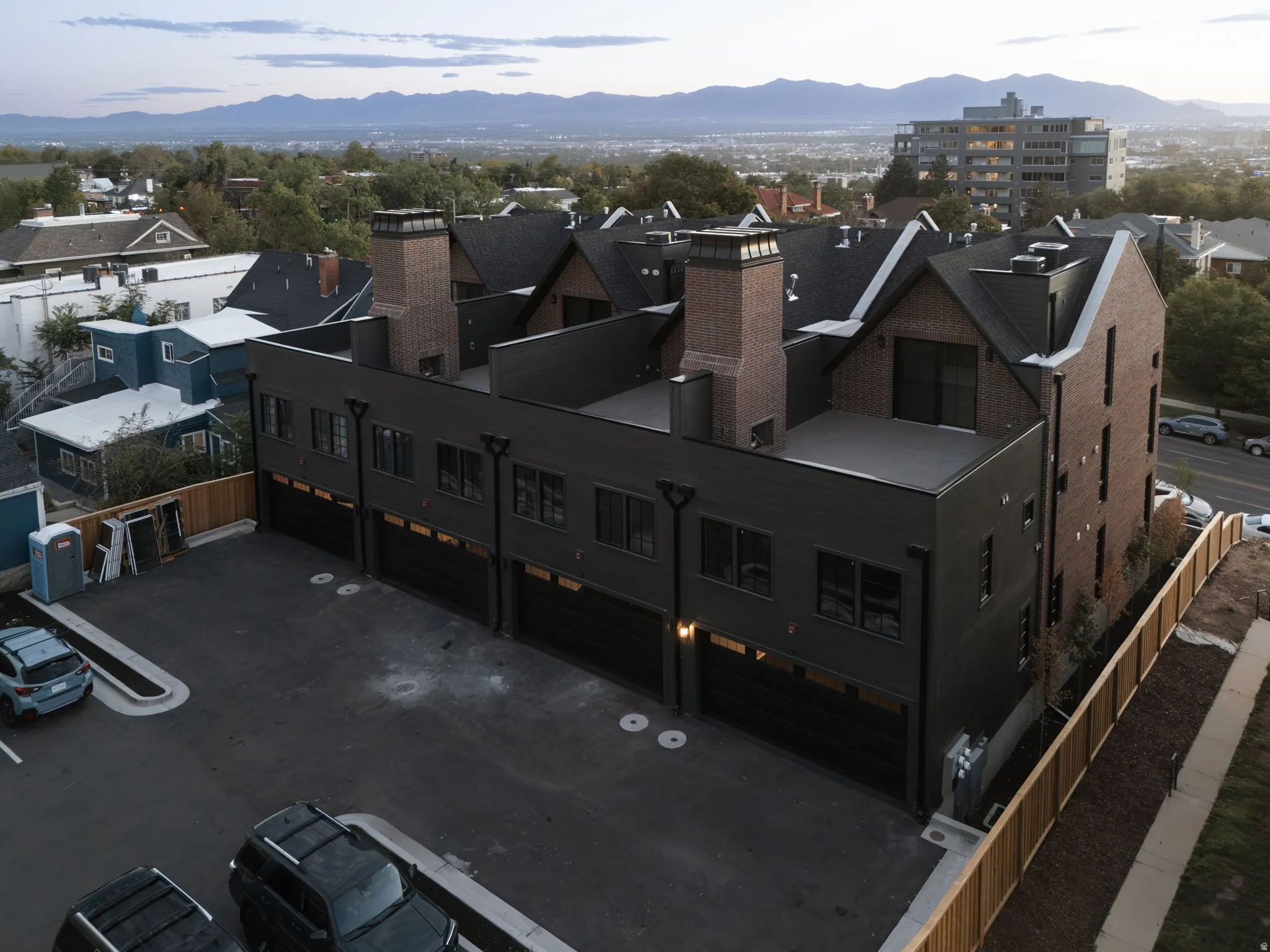 Contemporary townhome architecture featuring dark siding, brick accents, multiple garage bays, private rooftop patios, and a paved parking area