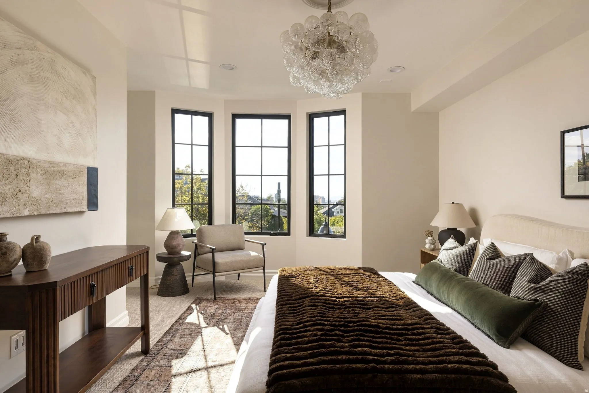 Coved ceiling with a contemporary glass chandelier, three black-framed windows, and light wood-finish flooring