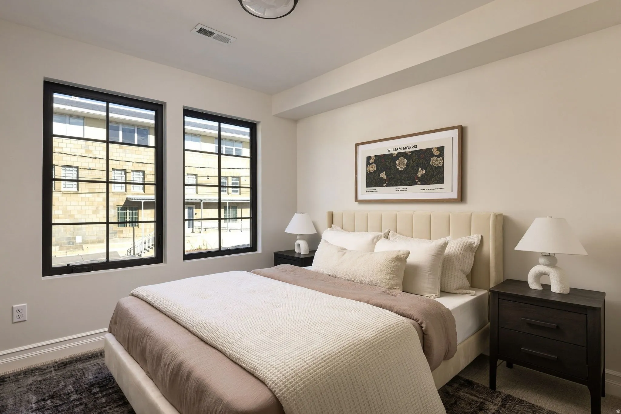 Two large windows with black grilles, light neutral wall paint, and a ceiling-mounted light fixture