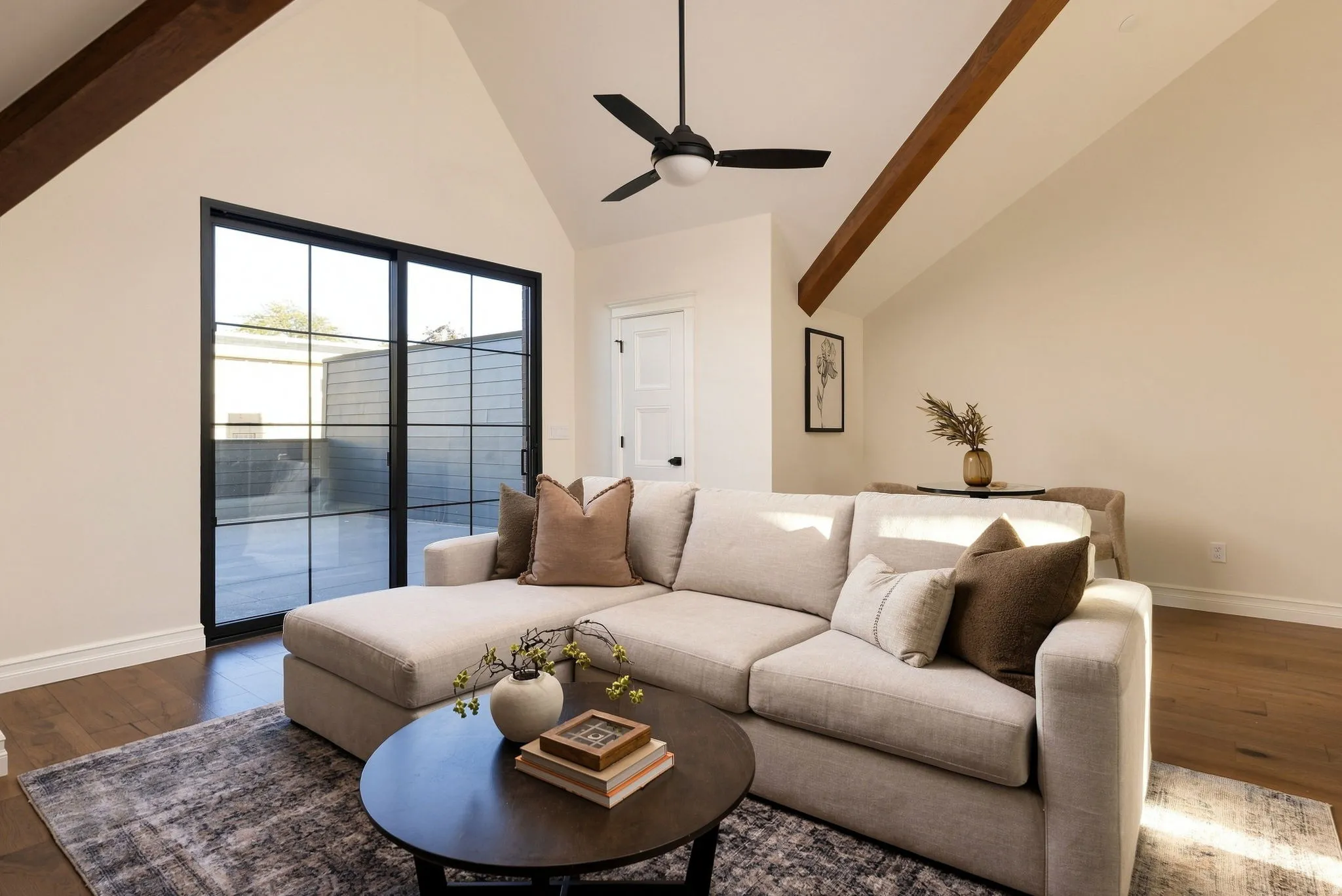 Vaulted ceiling with exposed wood beams, wood-finish flooring, and a contemporary ceiling fan