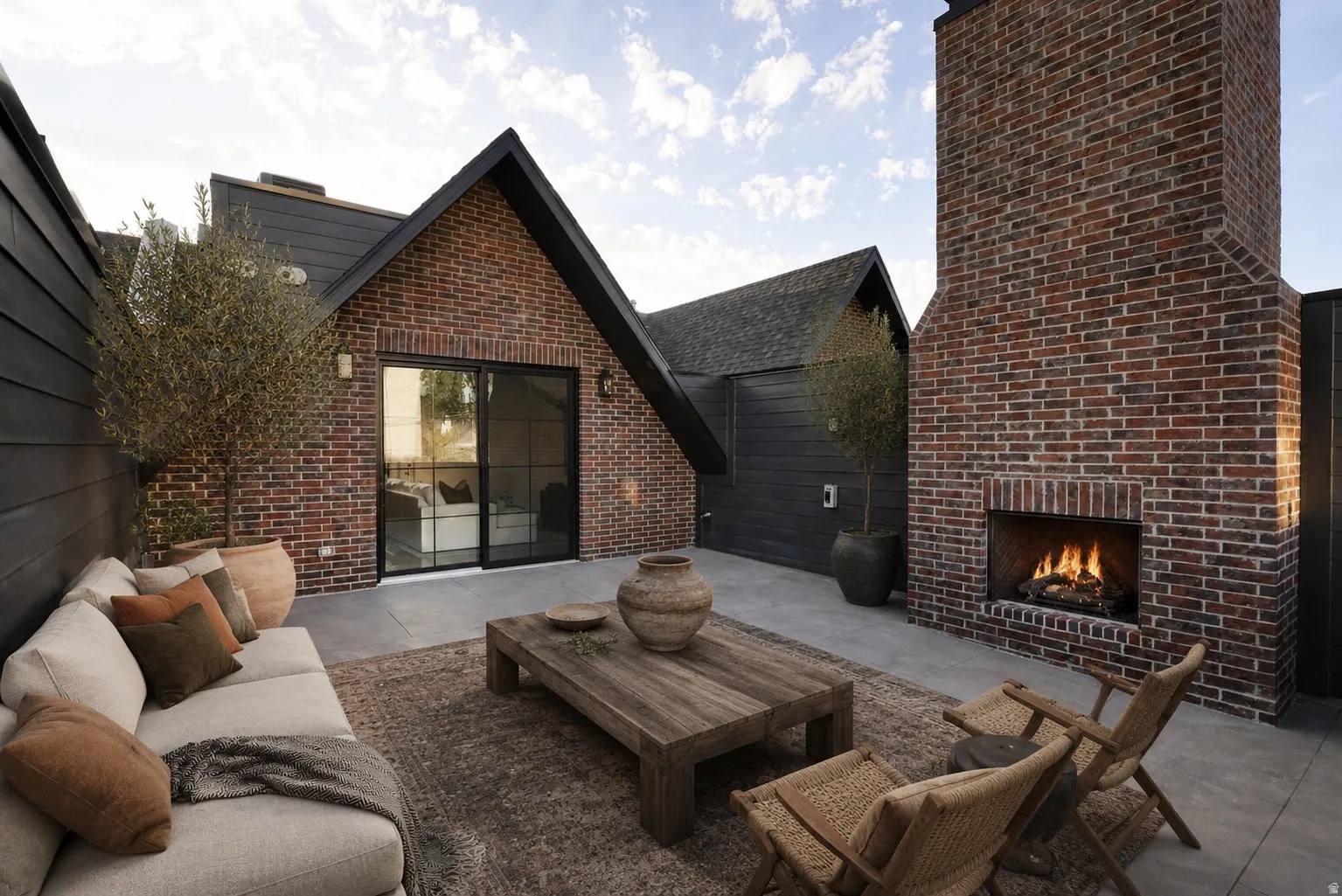 Exterior brick cladding, gabled roofline, black horizontal siding, outdoor fireplace, and sliding glass doors