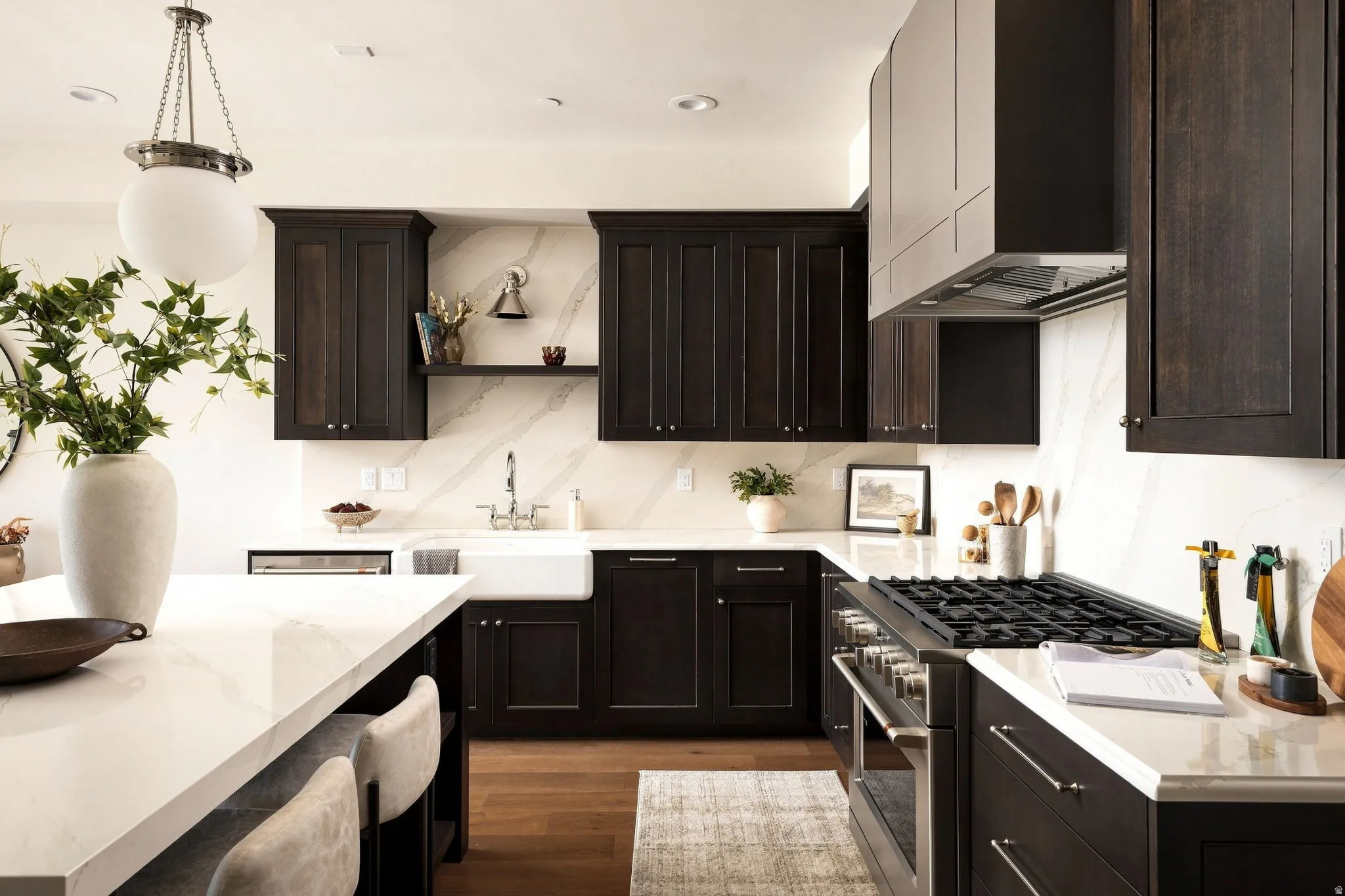 Kitchen featuring dark wood cabinetry, white stone countertops, farmhouse sink, stainless steel range with gas burners, and wood-finish flooring