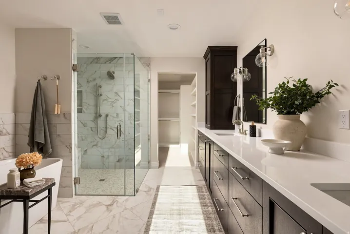 Spacious bathroom featuring a freestanding tub, glass-enclosed shower with tiled walls, dual vanity with undermount sinks, stone countertops, and dark wood cabinetry