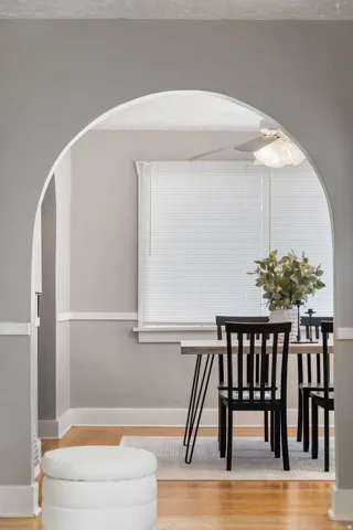 Archway entry to dining space with wood-finish flooring, white trim, and a window with blinds