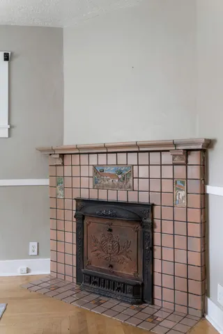 Fireplace featuring ceramic tile surround, decorative mantel, cast iron insert, and wood-finish flooring