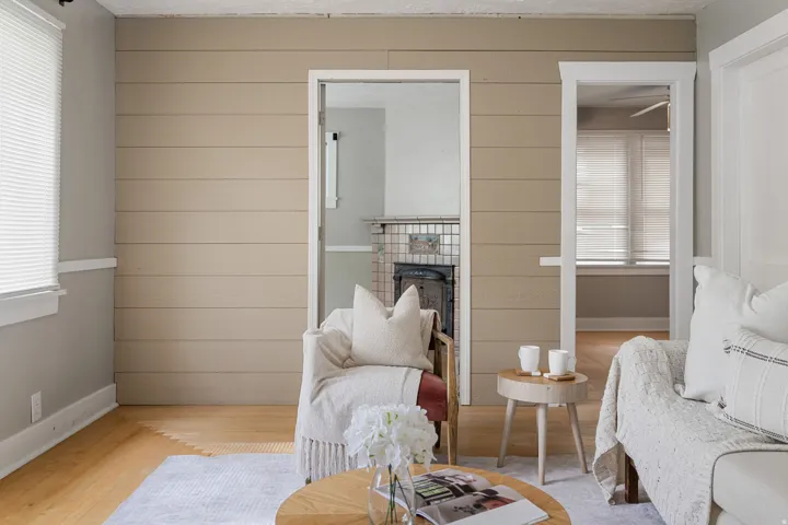Hardwood flooring, horizontal wood panel accent wall, white trim, cased openings, and a tiled fireplace surround