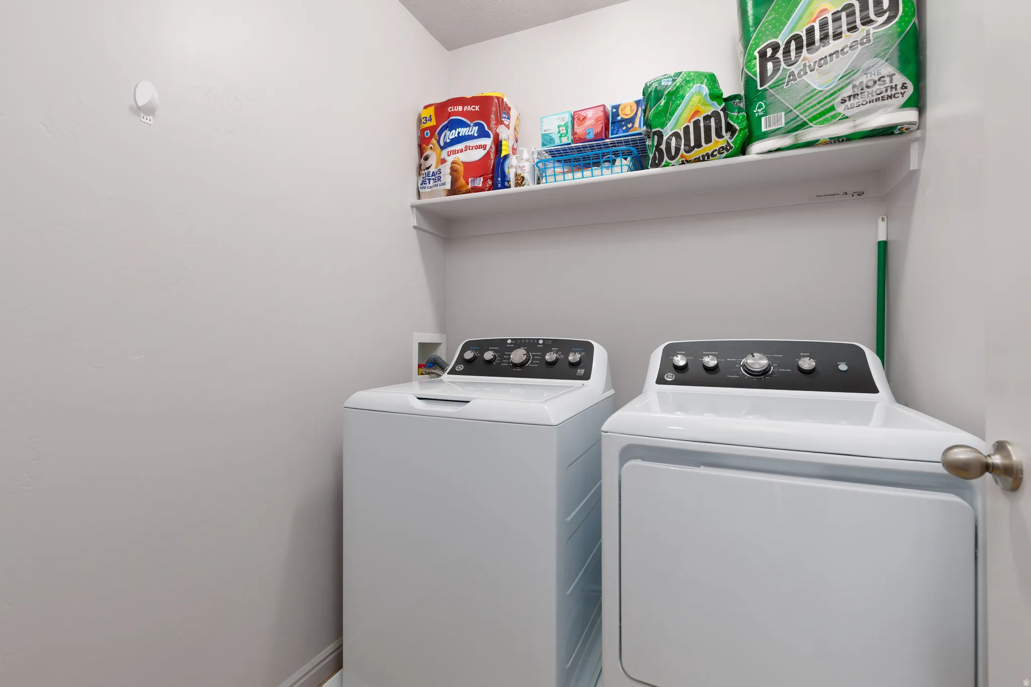 Laundry area featuring white appliances and an overhead storage shelf