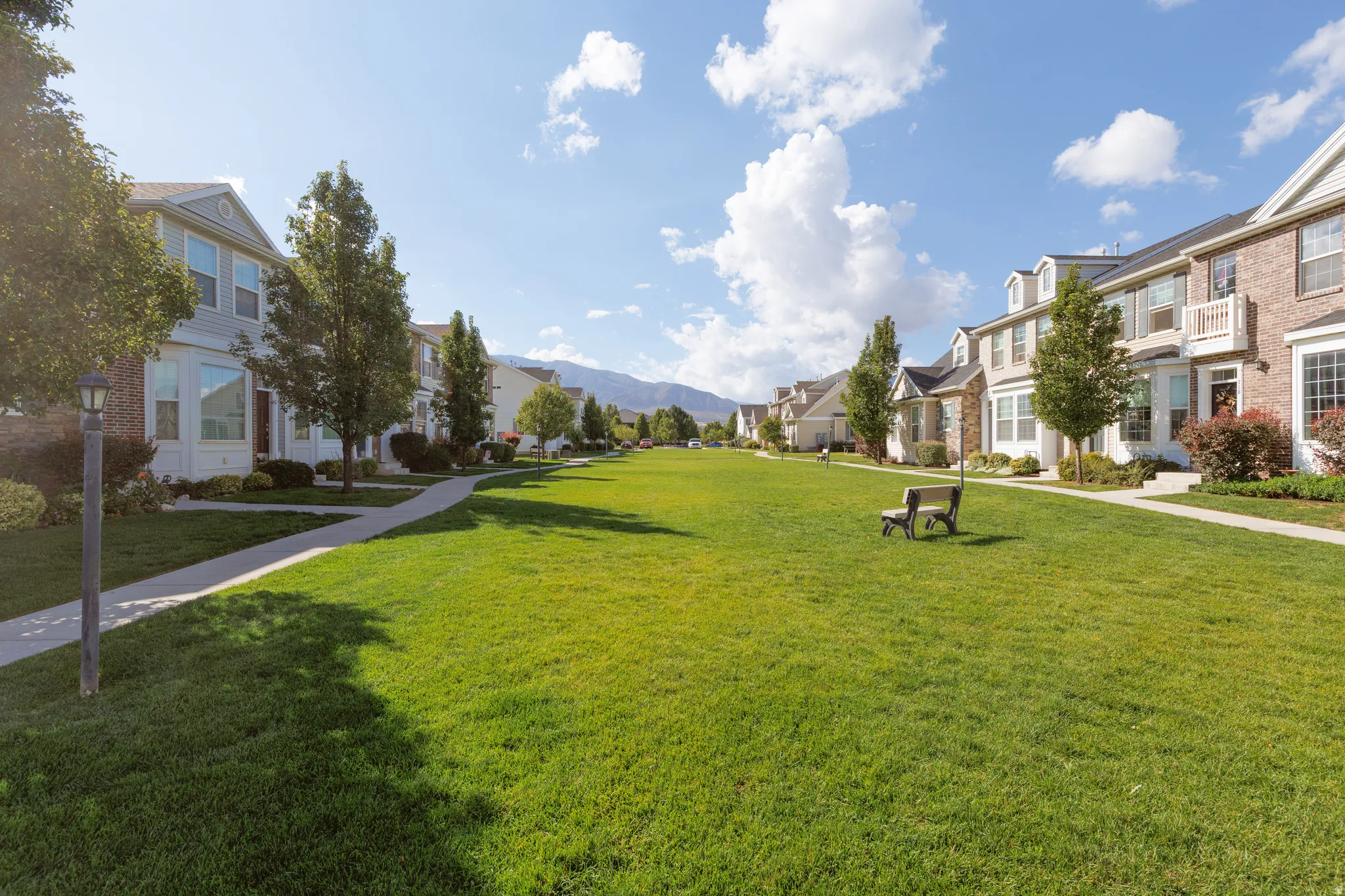 Expansive green space featuring a paved walkway, mature trees, and a mountain backdrop