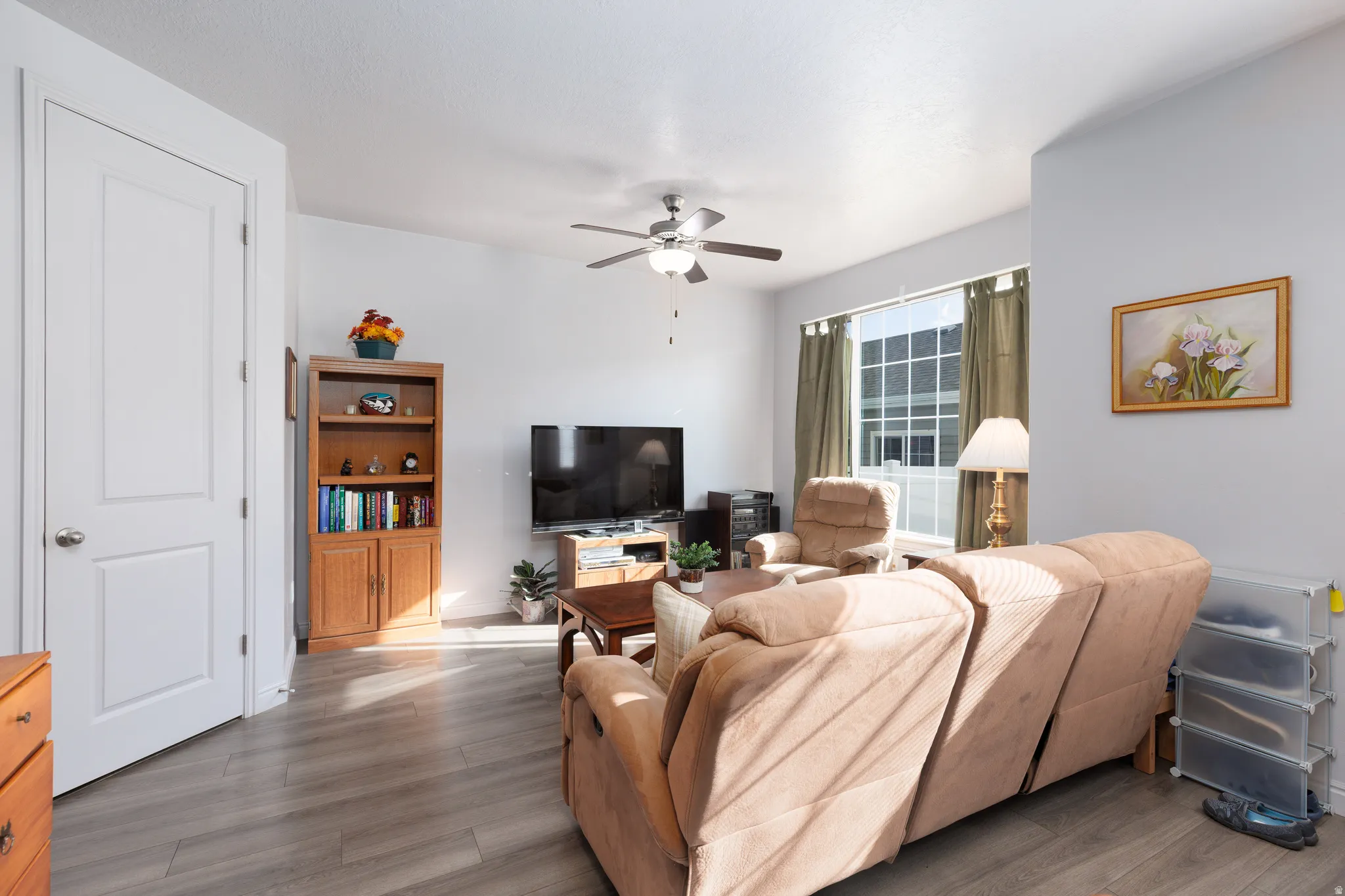 Spacious room featuring wood-finish flooring, a ceiling fan, and large windows with vertical blinds