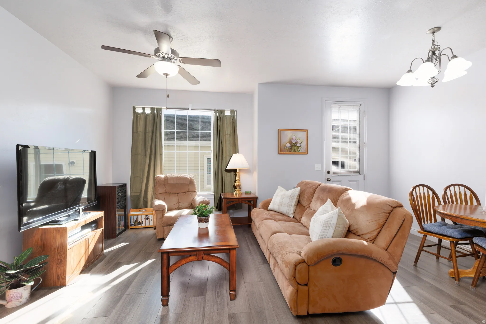 Open-concept living space featuring wood-finish flooring, a ceiling fan with integrated lighting, and a white paneled door