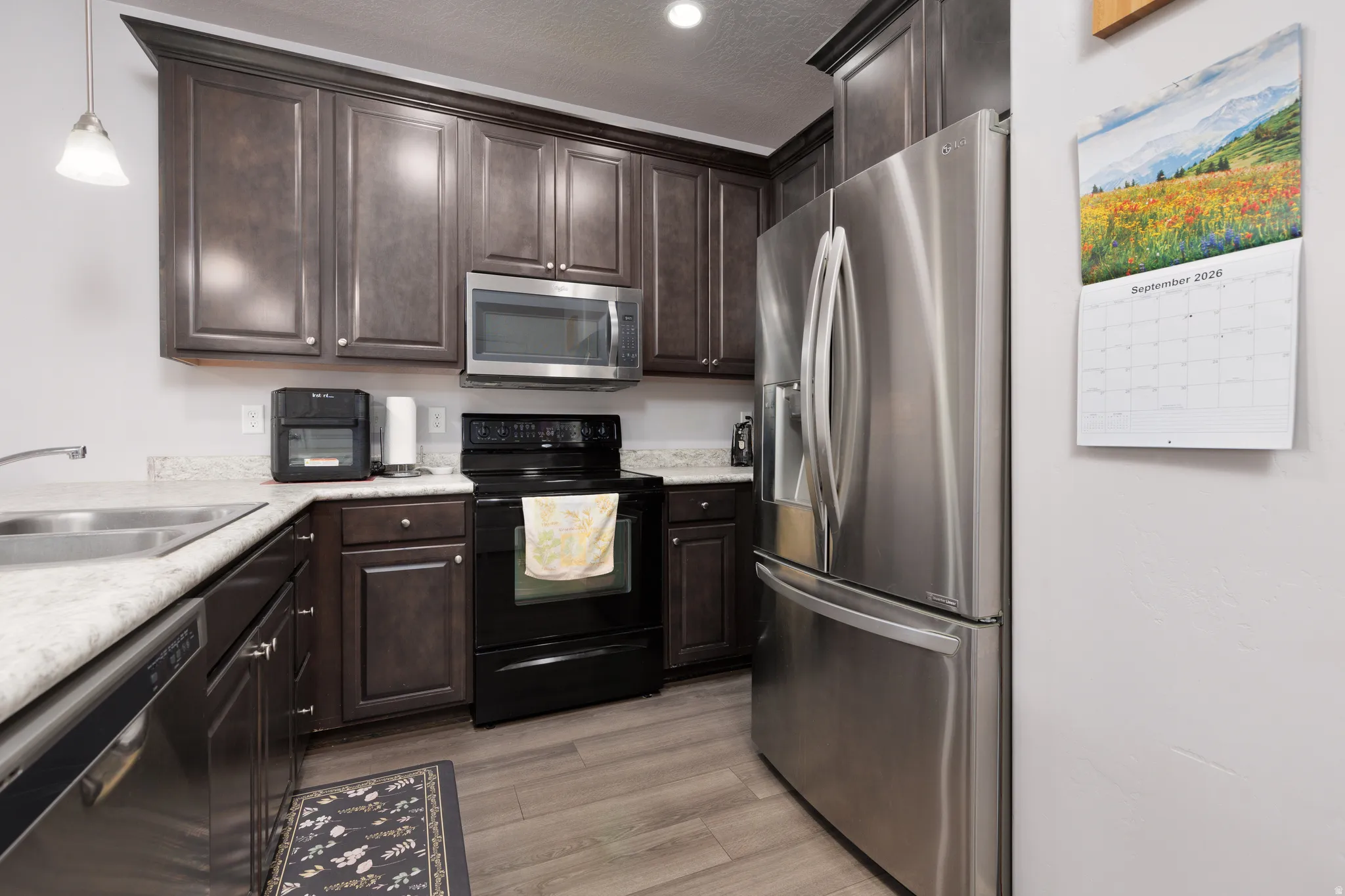 Kitchen featuring wood-finish flooring, dark wood cabinetry, light-toned countertops, a stainless steel refrigerator, and a stainless steel built-in microwave