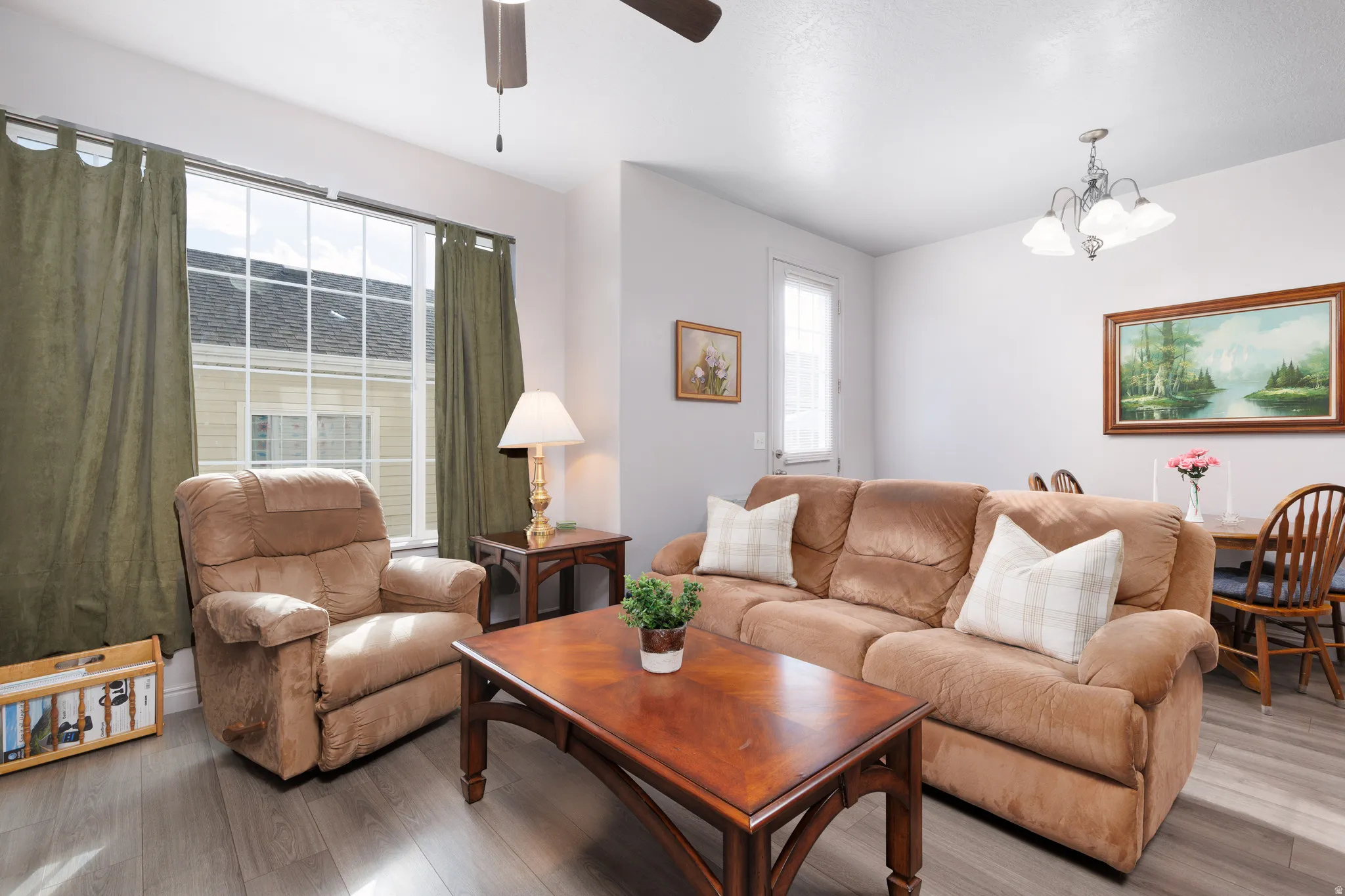 Open-concept living area with wood-finish flooring, a large window, and a ceiling fan