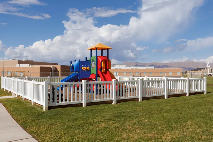 Manicured lawn area featuring a white picket fence enclosing a colorful playground structure with slides and platforms