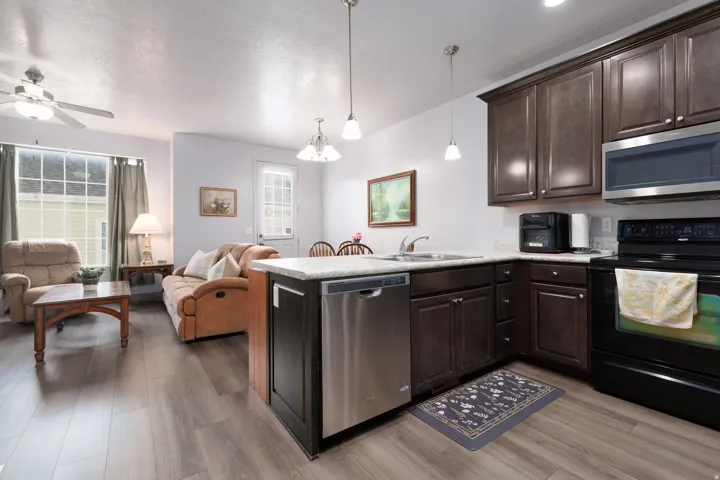 Wood-finish flooring throughout, dark wood-finish cabinetry, stainless steel dishwasher, built-in microwave, and ceiling fan