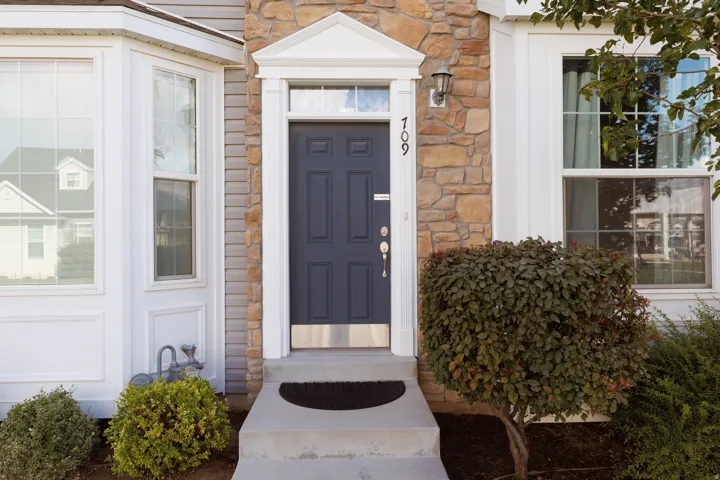 Stone veneer facade with a paneled front door, bay window, and exterior lighting fixture