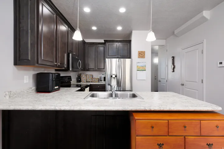 Kitchen island with a stainless steel sink, light-toned countertop, dark wood-finish cabinetry, and stainless steel appliances