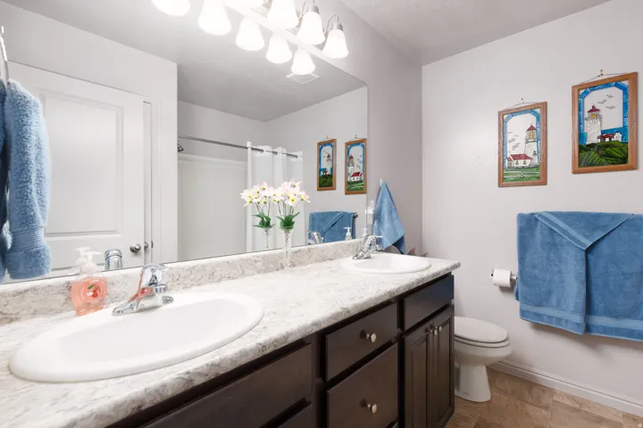 Double vanity with integrated sinks, a wide mirror, and dark wood-finish cabinetry