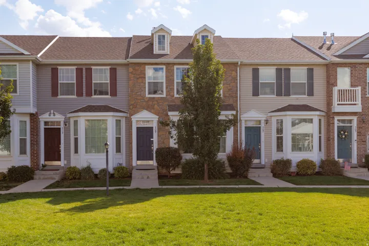 Townhome exterior with siding and stone facade, dormer windows, a bay window, and a gabled roof
