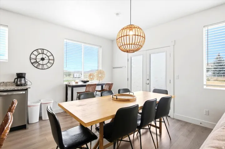 Wood-finish flooring, two large windows with blinds, a double glass-panel door, a stone-finish countertop, and a stainless steel dishwasher