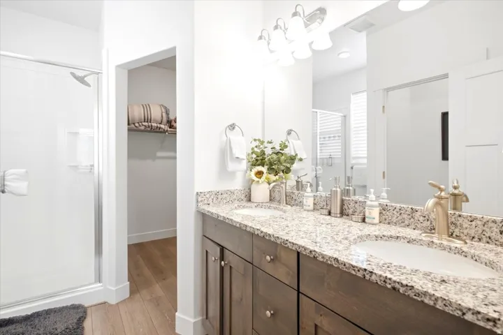 Dual vanity with granite countertop, integrated sinks, wood-finish cabinetry, and a walk-in shower with a glass enclosure