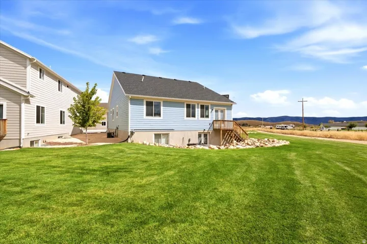 Expansive green lawn with a light blue siding exterior, white trim windows, and a wood deck with stairs