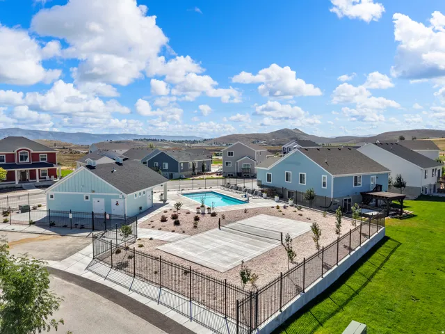 Community swimming pool with surrounding concrete patio, adjacent clubhouse building, and fenced outdoor court
