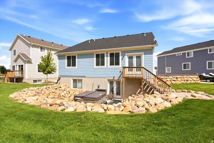 Rear exterior with light blue siding, a wooden deck with stairs, a hot tub, and a rock-lined landscaping feature