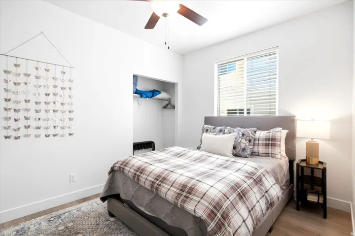 Recessed closet, ceiling fan, wood-finish flooring, and window with blinds