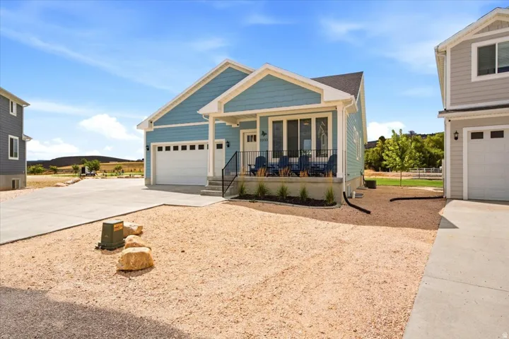 Light blue siding exterior with white trim, front porch with black railing, two-car garage, and concrete driveway