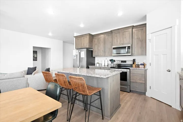 Kitchen featuring a central island with countertop seating, wood-finish flooring, stainless steel appliances, and gray cabinetry