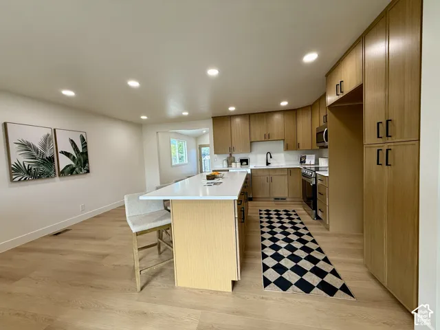 Open-concept kitchen featuring light wood-finish cabinetry, a large kitchen island with a light-toned countertop, and recessed lighting