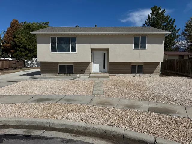 Split-level home featuring a stucco and brick facade, white entry door, multiple windows, and a gravel front yard with a concrete walkway