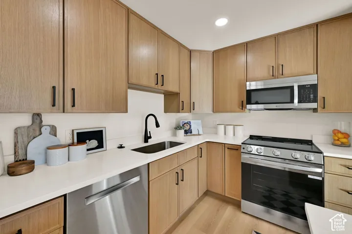 Light wood-finish cabinetry, stainless steel appliances, solid surface countertops, a matte black faucet, and wood-finish flooring