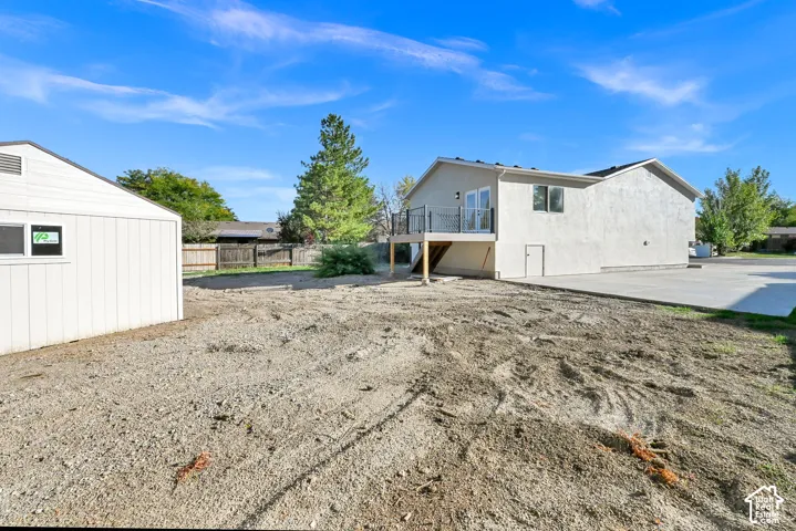Stucco exterior, elevated deck with dark railings, double glass doors, ground-level entrance, and concrete driveway
