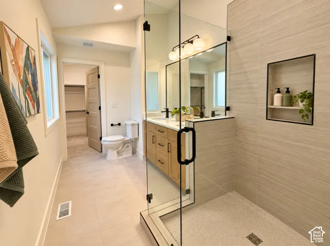 Walk-in shower with tiled walls and built-in niche, dual vanity with wood-finish cabinetry, and a separate water closet