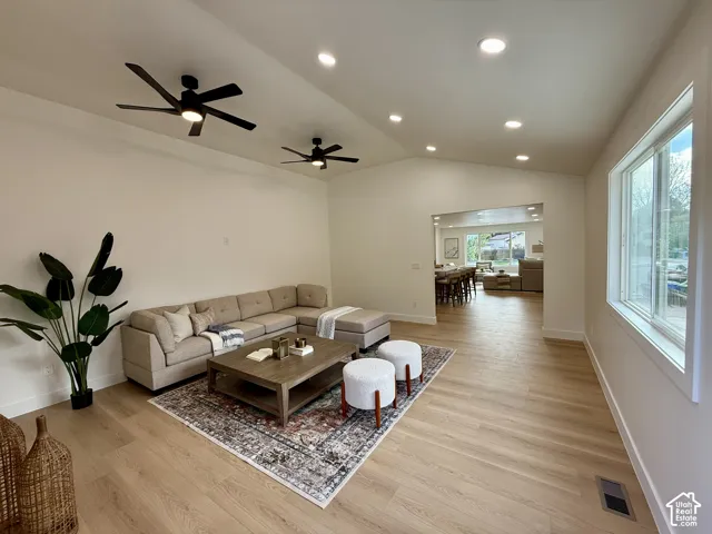 Vaulted ceiling with recessed lighting and two ceiling fans, wood-finish flooring, and large windows