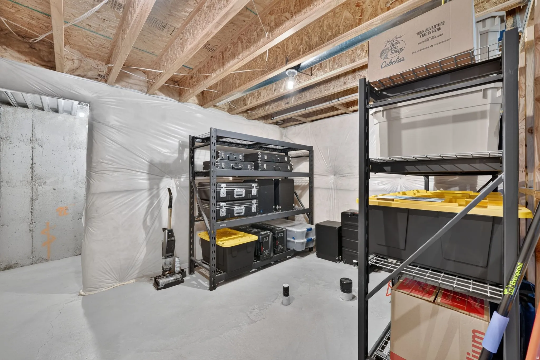 Exposed ceiling joists with insulation, concrete slab flooring, and built-in metal shelving