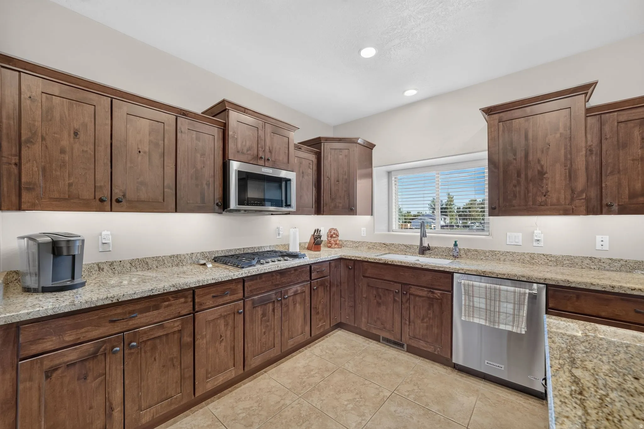 Kitchen featuring extensive wood cabinetry, light-toned granite countertops, stainless steel appliances, and a tile floor